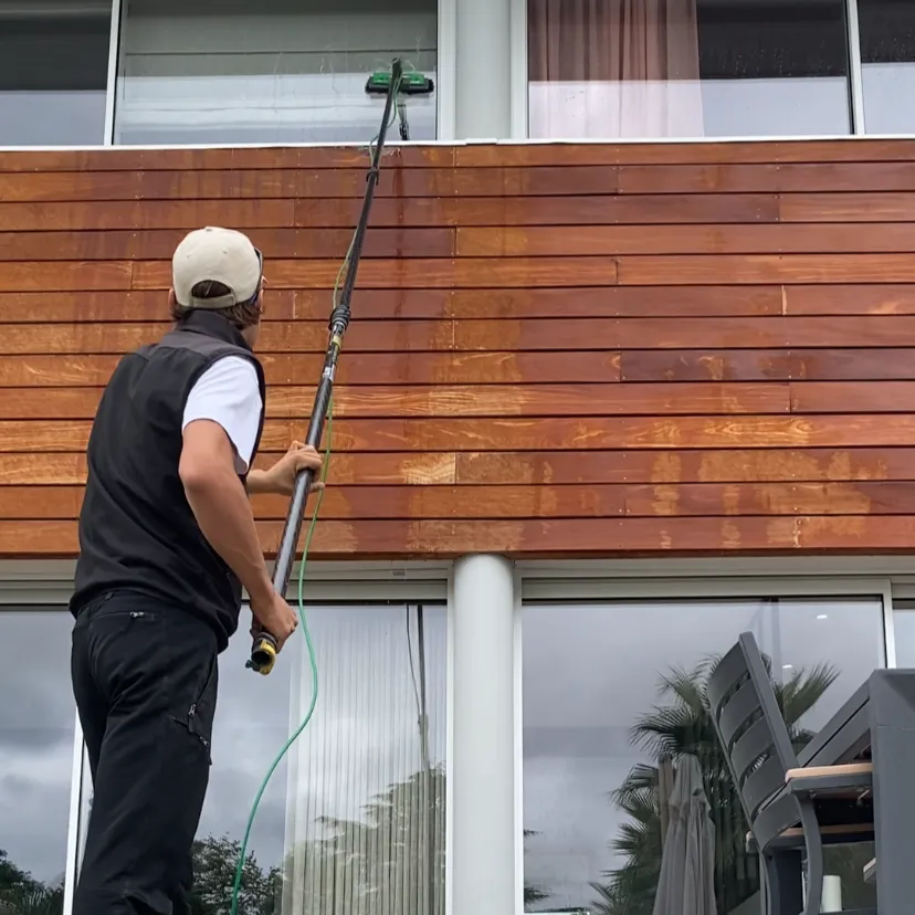 Technicien Toposmose en train de nettoyer une façade en bois avec une perche télescopique